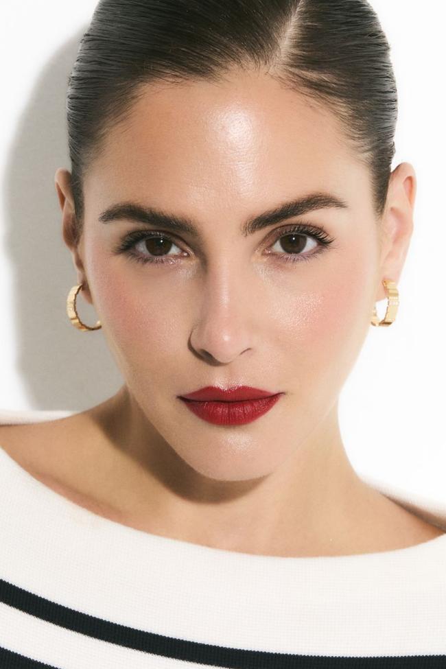 Andrea lleva mono de rayas de Dior y pendientes de oro de la colección GEM de Dior. En los labios, el rojo intenso se consigue con el mítico Rouge Dior en el tono 999, previamente delineado con el perfilador de labios Rouge Dior Contour en tono 999.